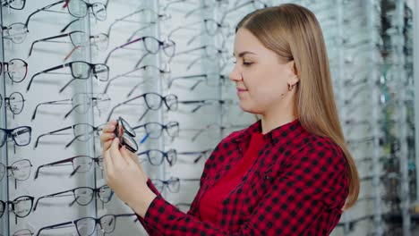 female customer in the optical store. beautiful young woman choosing new stylish eyeglasses in the shop. eyewear concept.