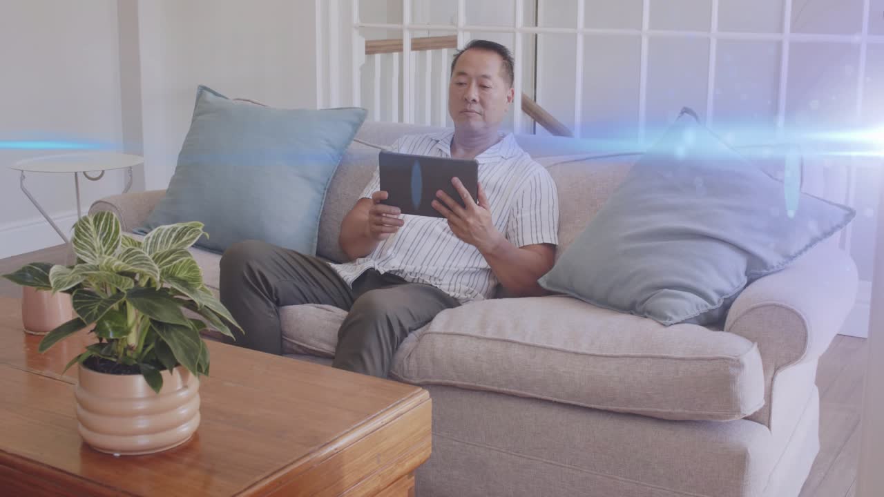 Man tapping tablet and shifting posture on sofa, tech demo showing bluish light streak overlay