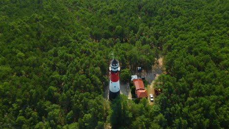 drone spinning around stilo lighthouse and green forest- lighthouse located in osetnik on the polish coast of the baltic sea, close to the village of sasino, aerial