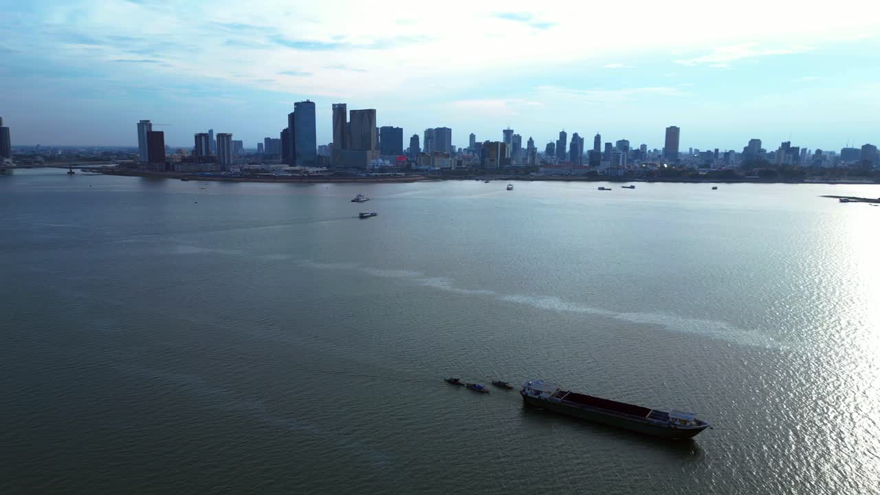 Cargo ship sailing on the Mekong river near Phnom Penh skyline in Cambodia. Spectacular aerial view flight static tripod hovering drone
