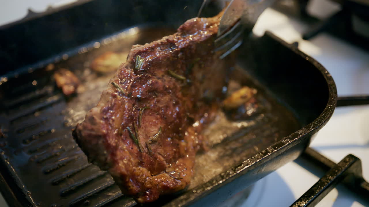 Close up of a juicy steak sizzling in a grill pan while being pressed with a spatula