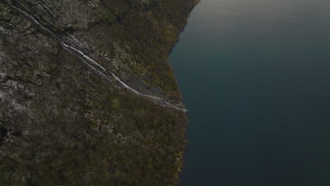 De-Arriba-Hacia-Abajo-De-La-Cascada-Que-Fluye-Desde-Las-Escarpadas-Montañas-Rocosas-En-El-Fiordo-En-La-Costa-Oeste-De-Noruega