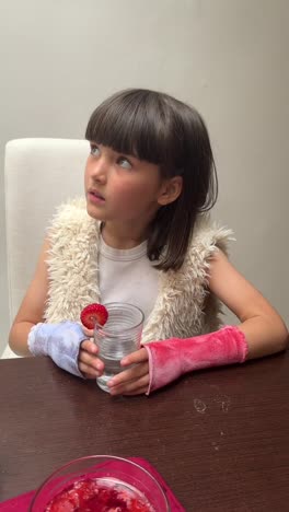 young girl drinking water with strawberry slice, wearing arm braces