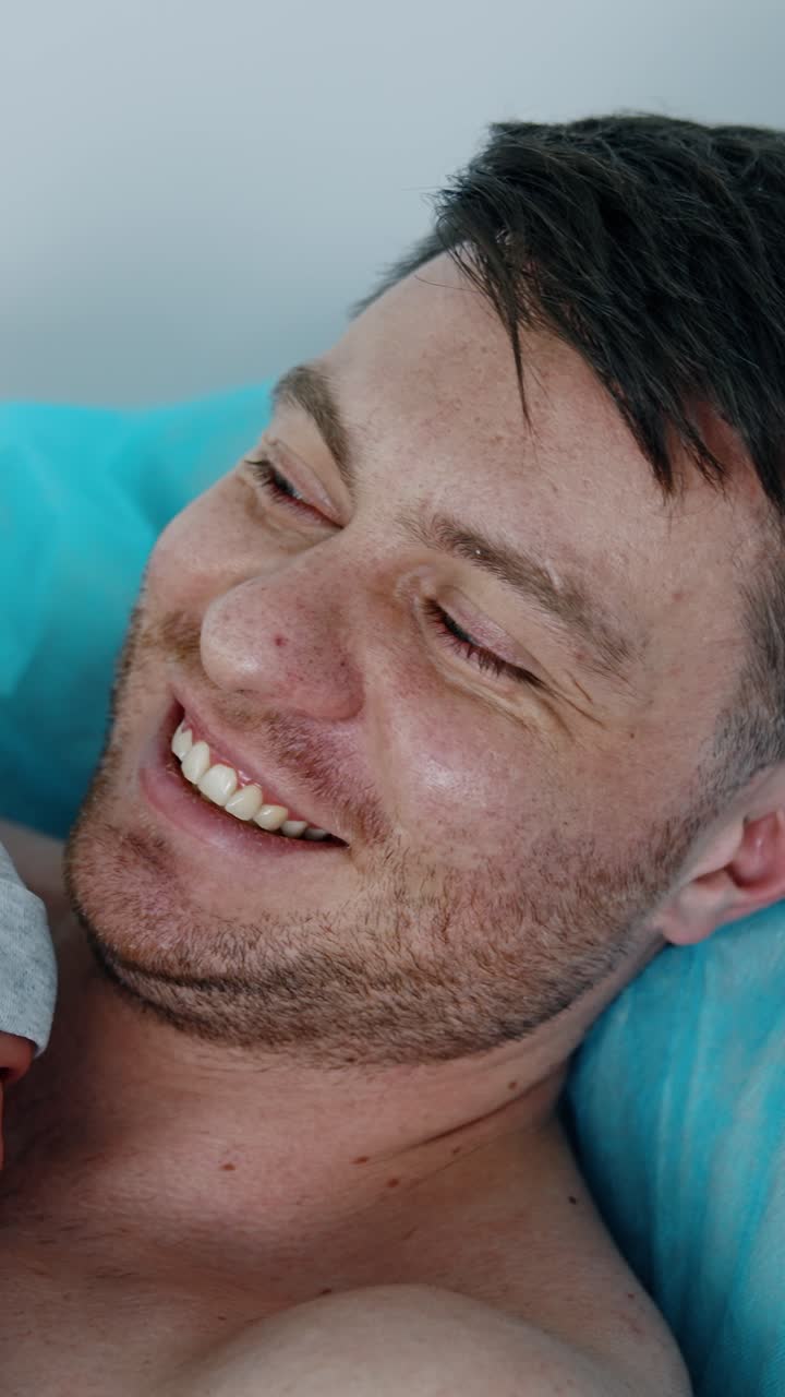 Uomo caucasico felice è emozionato di tenere in braccio il suo neonato. Il padre ha le lacrime agli occhi mentre tiene con cura il figlio. Vista dall'alto. Video verticale.