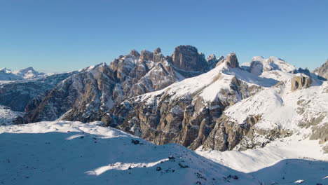 Idyllic-harsh-snowy-alps-valley-landscape-elevated-aerial-view-rising-above-sunlit-mountain-terrain