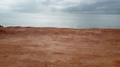 Retroceda-Desde-El-Acantilado-Del-Lado-De-La-Playa-Brasileña-Hacia-La-Silueta-De-Una-Persona-Sola-Sentada-En-El-Acantilado