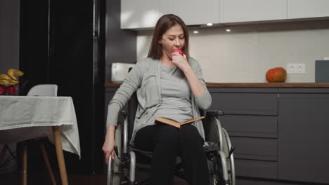 woman in wheelchair reads book and eats apple resting alone