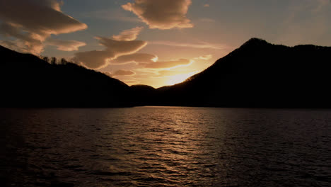 Tiro-Bajo-Aéreo-De-Alto-Contraste,-Volando-Sobre-Un-Lago-De-Montaña,-Hacia-El-Sol-Y-Hermosas-Nubes,-Pacífico,-Sereno