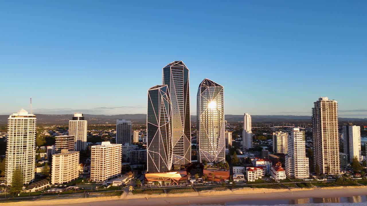 Drone captures Gold Coast skyline at sunrise, highlighting skyscrapers and beach. Warm lighting creates a serene, vibrant atmosphere