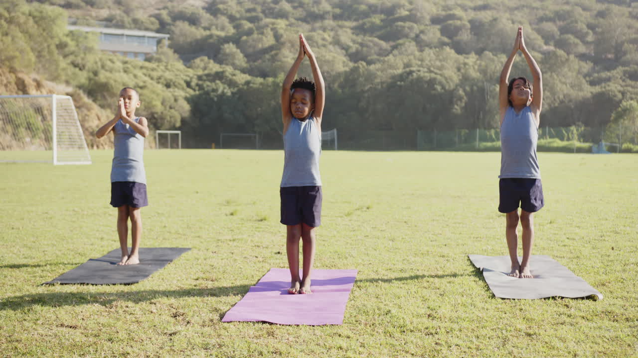 Practicing yoga on mats, three kids stretching outdoors at school field