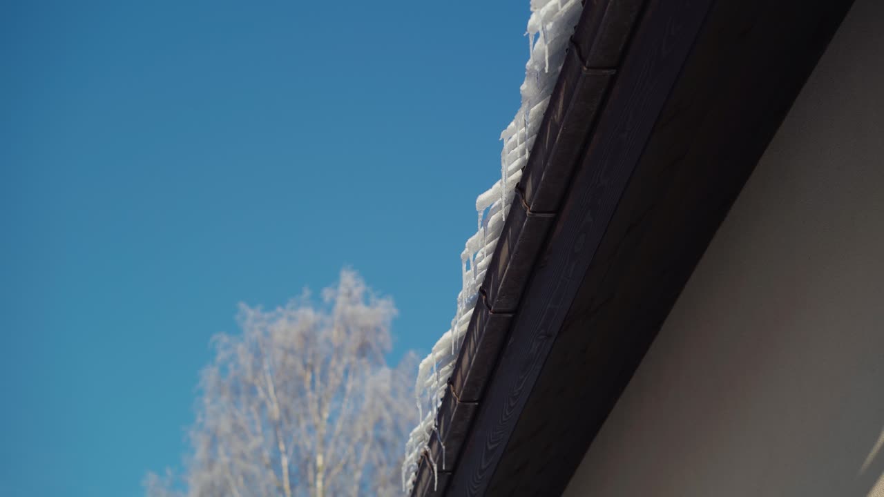 Frozen snow hanging over a roof. Icicles on a roof in a sunny and cold winter day.