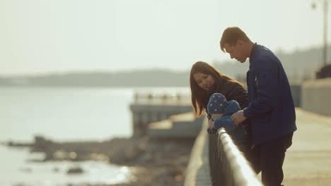 familia internacional feliz se encuentra en el parapeto en el muelle en la primavera. mujer coreana camina con su marido y hijo pequeño en el parque. movimiento circular de la cámara.
