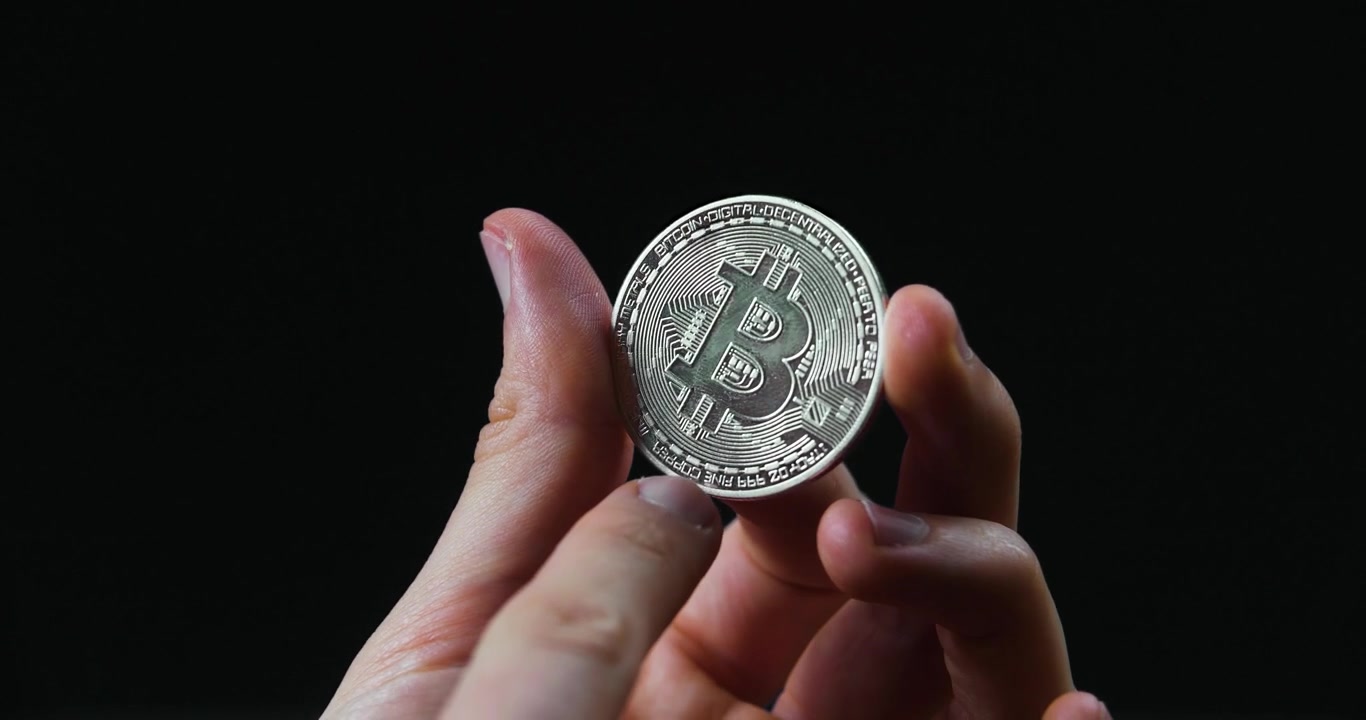 Siyah arka planda gümüş bir Bitcoin gösteren ellerin yakın çekimi