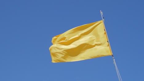 yellow flag waving in the wind against clear blue sky, slow motion low angle shot