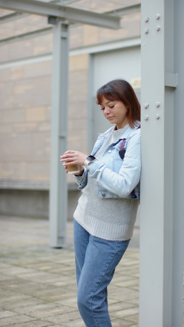 Video verticale: donna che entra in un cortile sorseggiando un caffè e controllando l'ora sullo smartwatch, spazio per il testo