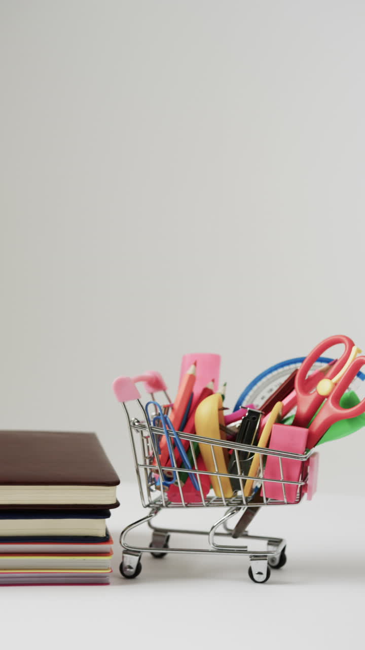 Vertical video of close up of shopping trolley with school items and books on grey background