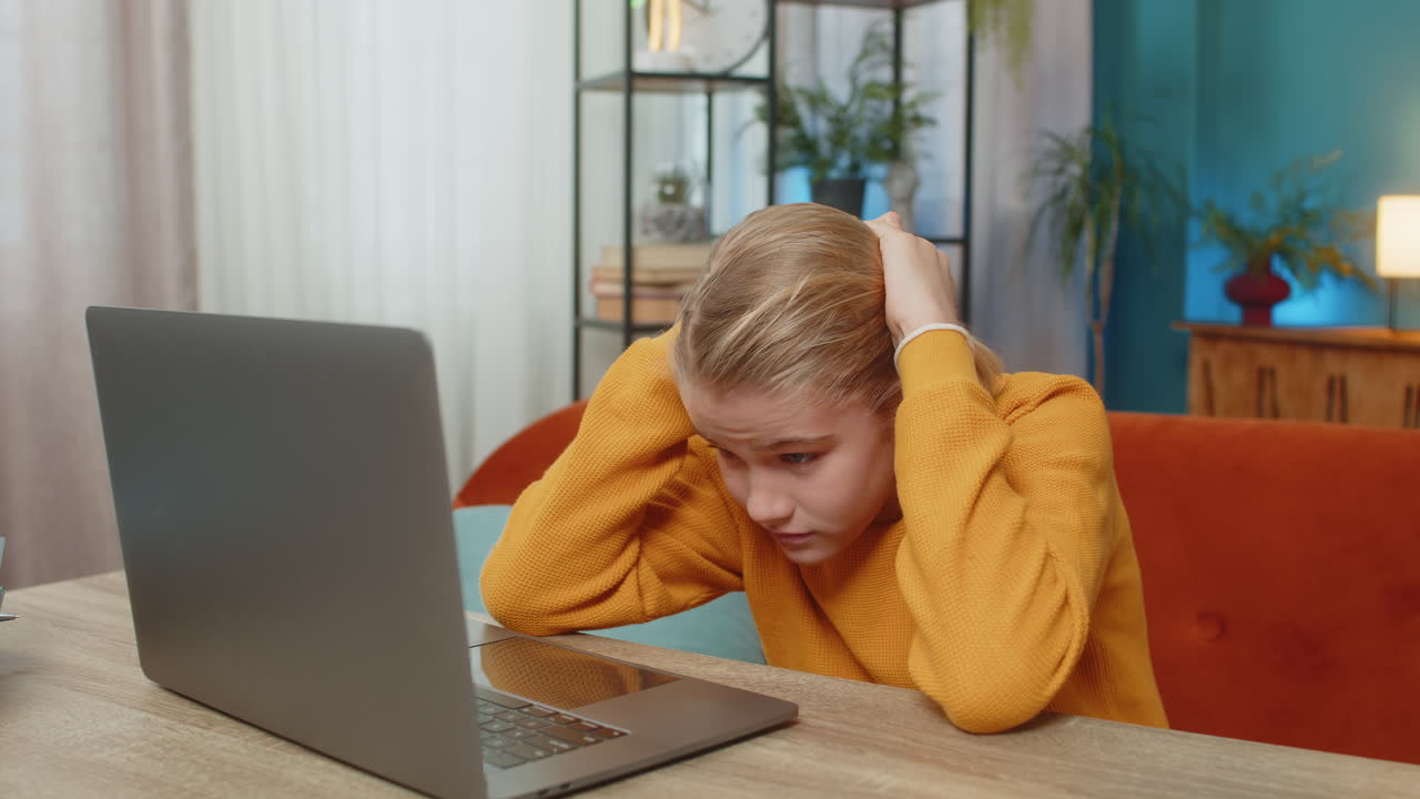Teenager boy frustrated playing difficult video game on laptop banging keyboard on couch at home