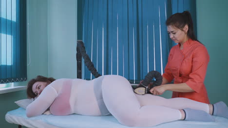 esteticista en uniforme hace masaje de vacío de la pierna de una chica regordeta