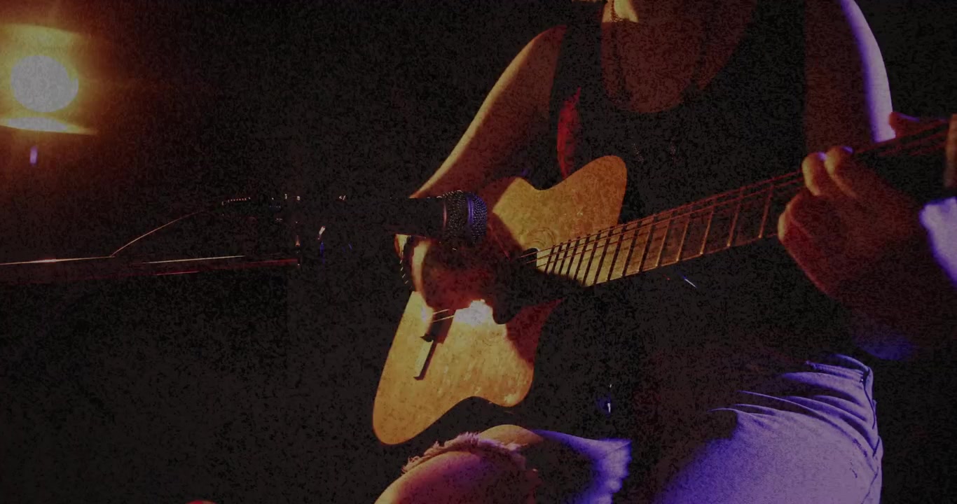 Giovane musicista sotto i riflettori che esegue fingerpicking sulla chitarra acustica.