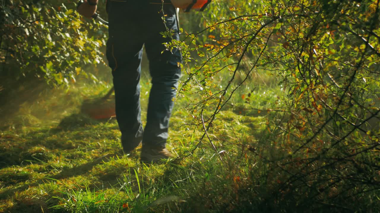 planta de jardín con un trabajador masculino que mantiene una cortadora eléctrica y corta hierba en el fondo