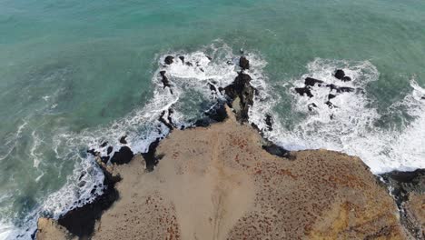 Aerial-Top-Down-Ocean-sandy-cliffs-in-white-foam-beach,-blue-waves-crush-shore