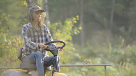 lady on ride-on mower in countryside wearing mosquito head, rack focus