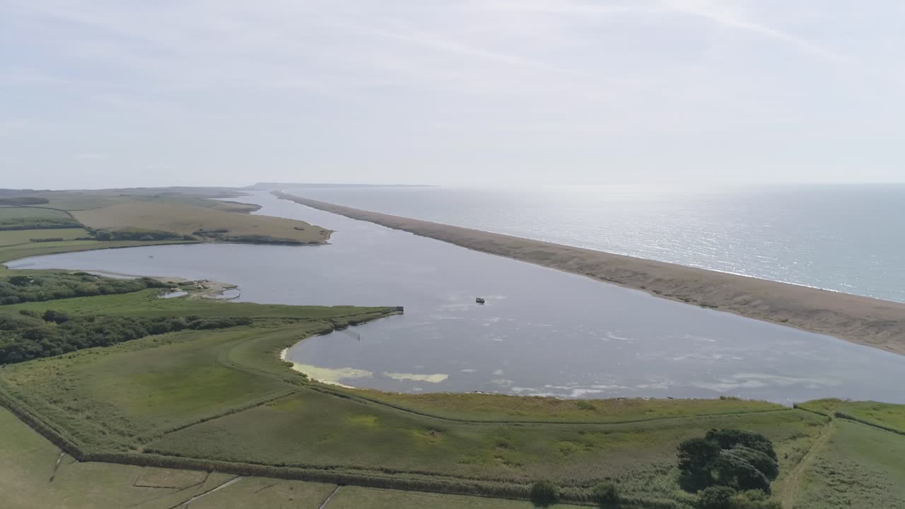 Ripresa aerea con movimento da destra a sinistra lungo Chesil Beach e la laguna Fleet, ruotando l'inquadratura verso il mare e il sole nascente