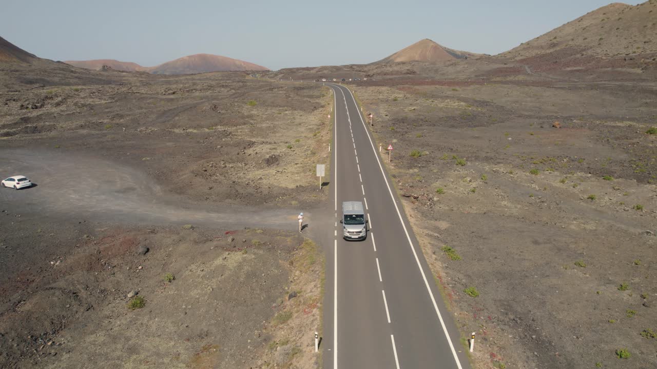 Vista aerea dall'alto che segue il furgone sulla strada che attraversa un vasto e arido paesaggio desertico, registrato in Spagna, Isole Canarie, Lanzarote, Isla Graciosa