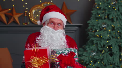 senior grandfather parodies santa claus presenting christmas gift box, holidays celebration at home