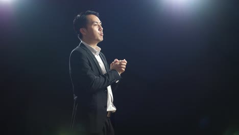 side view of asian speaker man in business suit holding his hands together while speaking in the black screen studio
