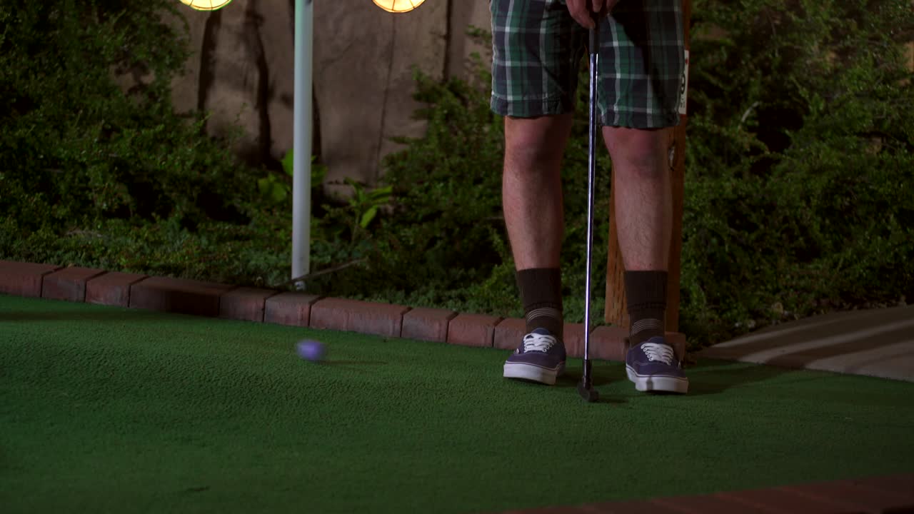 A close up of a purple mini golf ball getting hit with a club and the shot is horrible