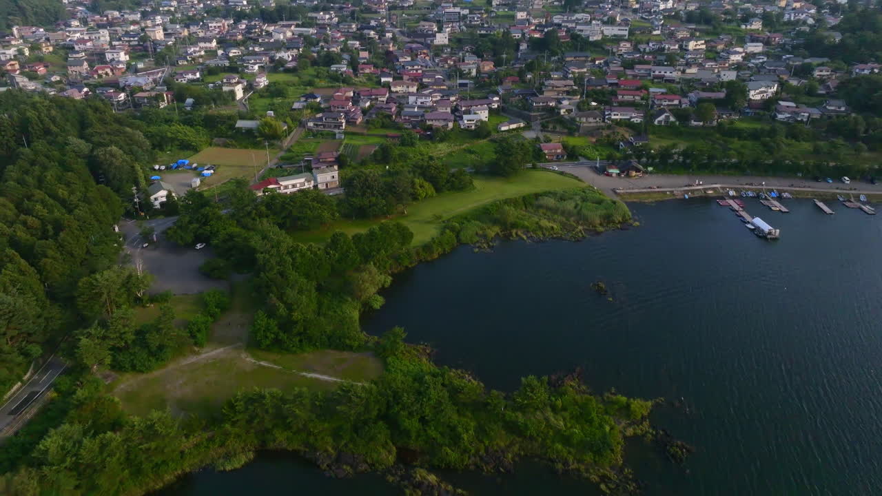 Aerial tilt reveal of Fujikawaguchiko city and Mount Fuji, golden hour in Japan