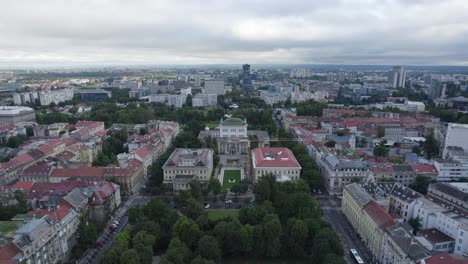 Establishing-aerial-view-of-Croatian-national-theatre,-Zagreb,-reverse-over-Mažuranić-square-urban-public-gardens