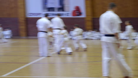little sportsmen split into pairs to practice karate fight. coaches watch every pair of athletes. other kids waiting for their turn sitting on the floor at backdrop.