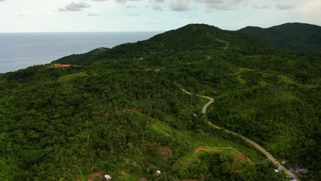 Aerial flyover shot of serpentine road amid lush tropical jungle and mountains at Baras, Catanduanes, Philippines