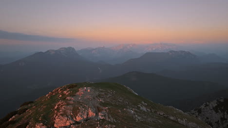 Eine-Drohnenaufnahme-Von-Der-Spitze-Des-Berges-Peca-Am-Frühen-Morgen,-Hellorange-Farben-Am-Himmel,-Ein-Wanderer-Steht-Oben