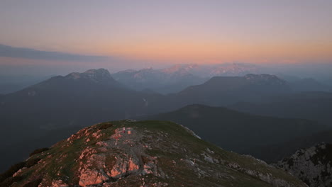 a drone shot of the top of mountain peca in the early morning, light orange colors in the sky, one hiker standing at the top