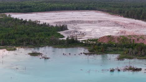 aerial drone footage of a turquoise water quarry bordered by forest and a large exposed rocky mining area