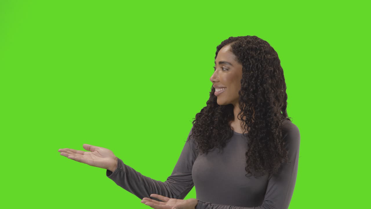 Portrait Of Woman Presenting Or Demonstrating Item Against Green Screen Smiling At Camera 1