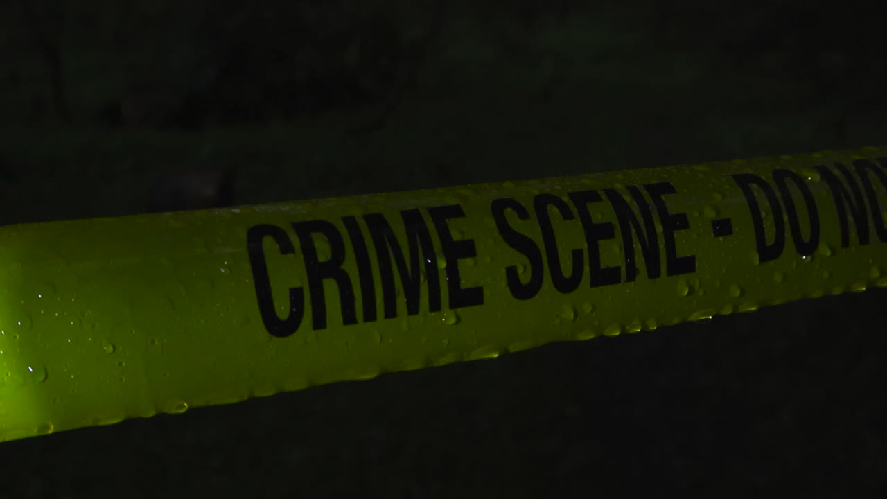Slow motion video of raindrops and water drops falling on a forensic police tape ribbon during night time. The water is flowing and dropping off from the yellow colored crime scene tape