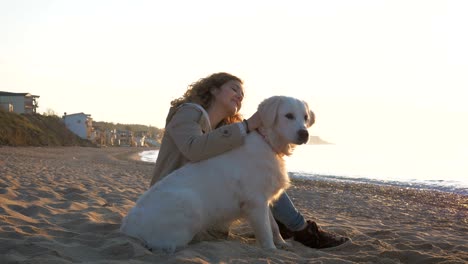 young female fast playing with retriever dog on the beach at sunset