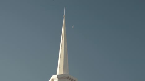 white spire from church building in blue sky with faint half moon in the background 4k