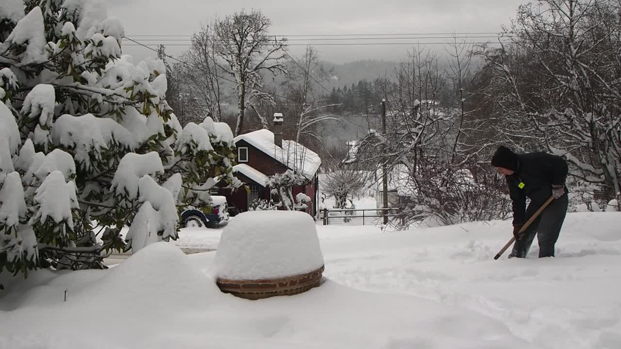 Man shoveling snow in Canada with trees and mountains in background