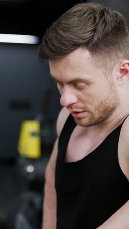 tired sportsman after workout. young handsome muscular guy standing near the simulator in the gym and having a rest. sportive lifestyle. vertical video