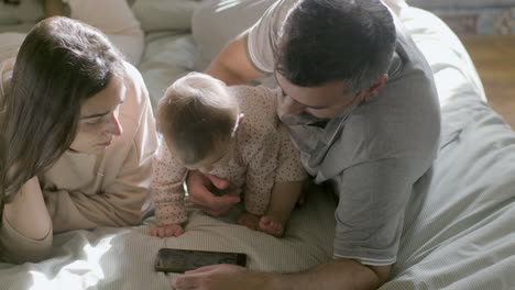 padres amorosos y su linda niña acostada en la cama y viendo dibujos animados en una tableta digital el domingo por la mañana 1