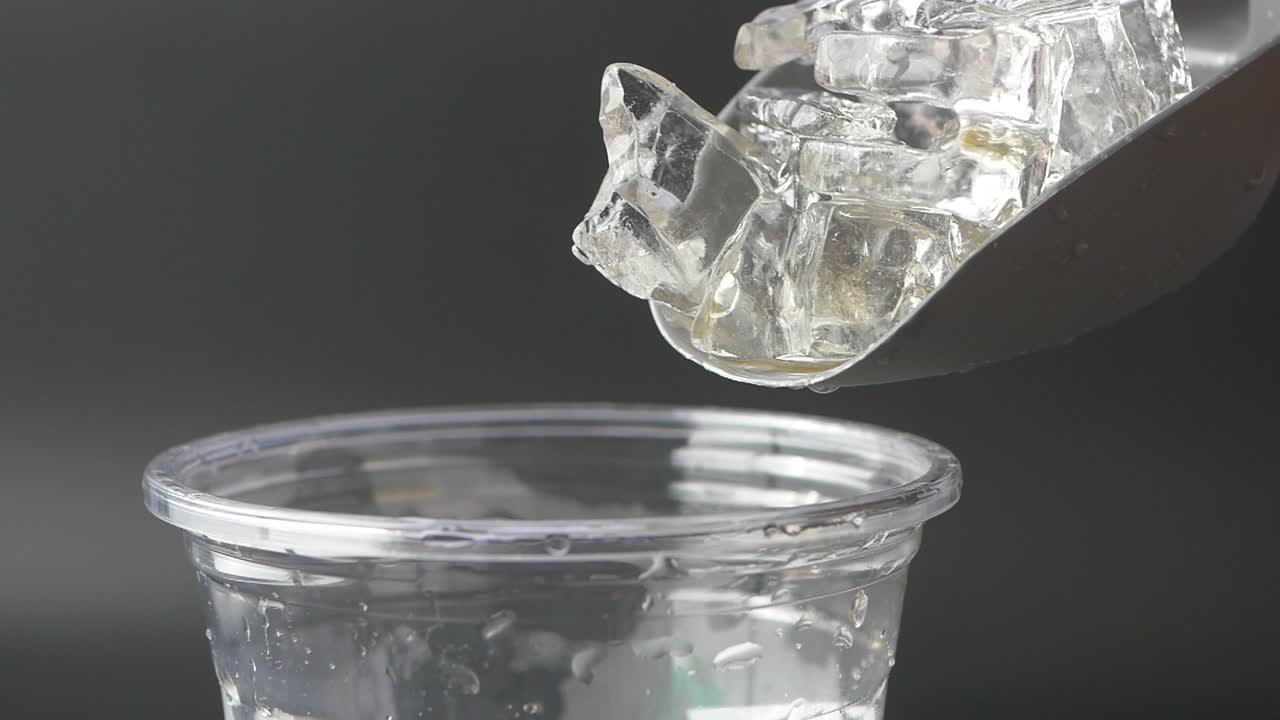 cubos de hielo siendo vertidos en una taza de plástico