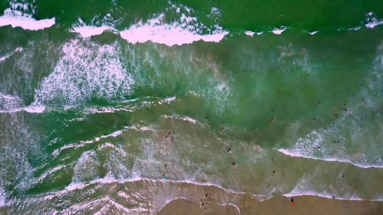 toma aérea de arriba hacia abajo de las olas del mar rompiendo en la playa y la gente en el agua