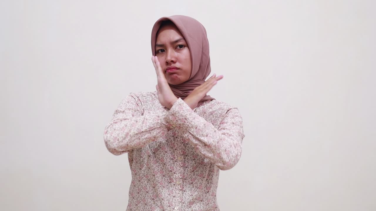 Young asian muslim girl standing while making prohibition gesture with crossed hands
