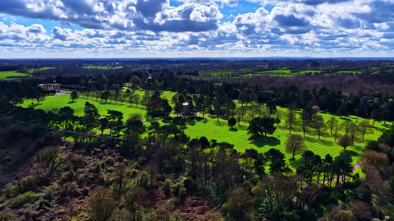 Luftfoto fra drone af en amerikansk militærkirkegård fra Anden Verdenskrig med hvide gravsten blandt grøn skov. Normandiet, Frankrig