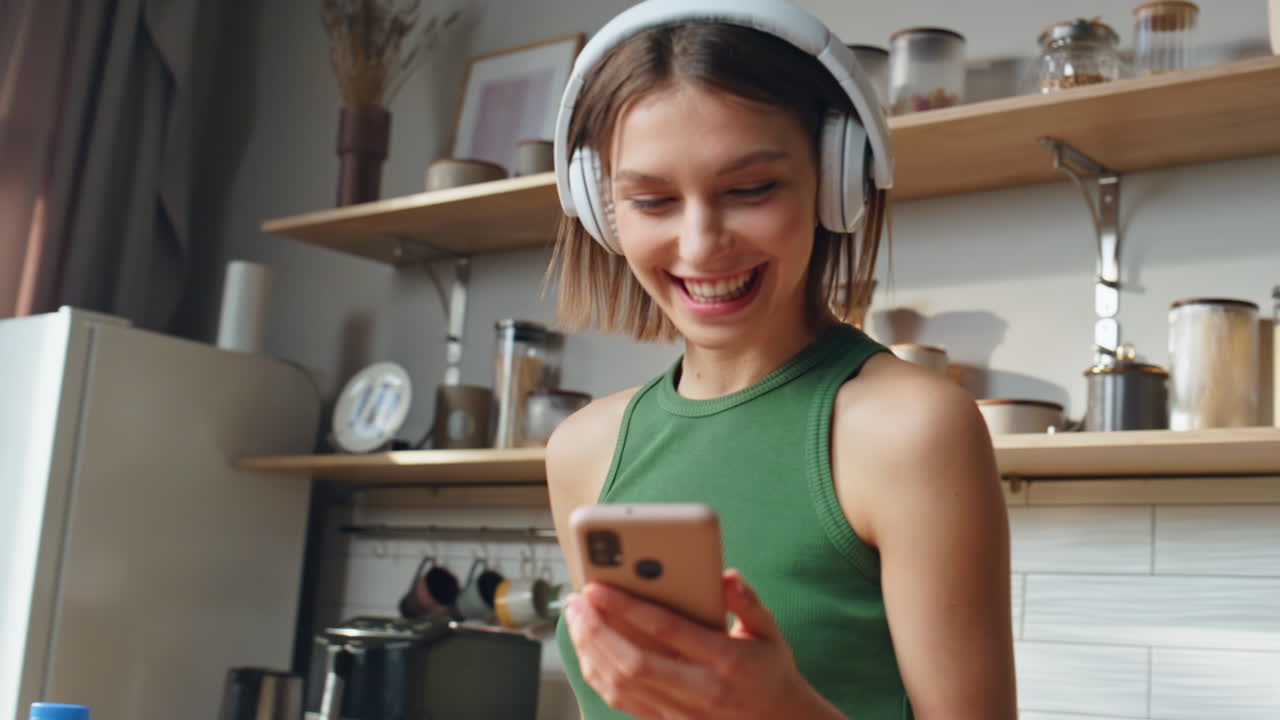 Woman with headphones using her phone in the kitchen